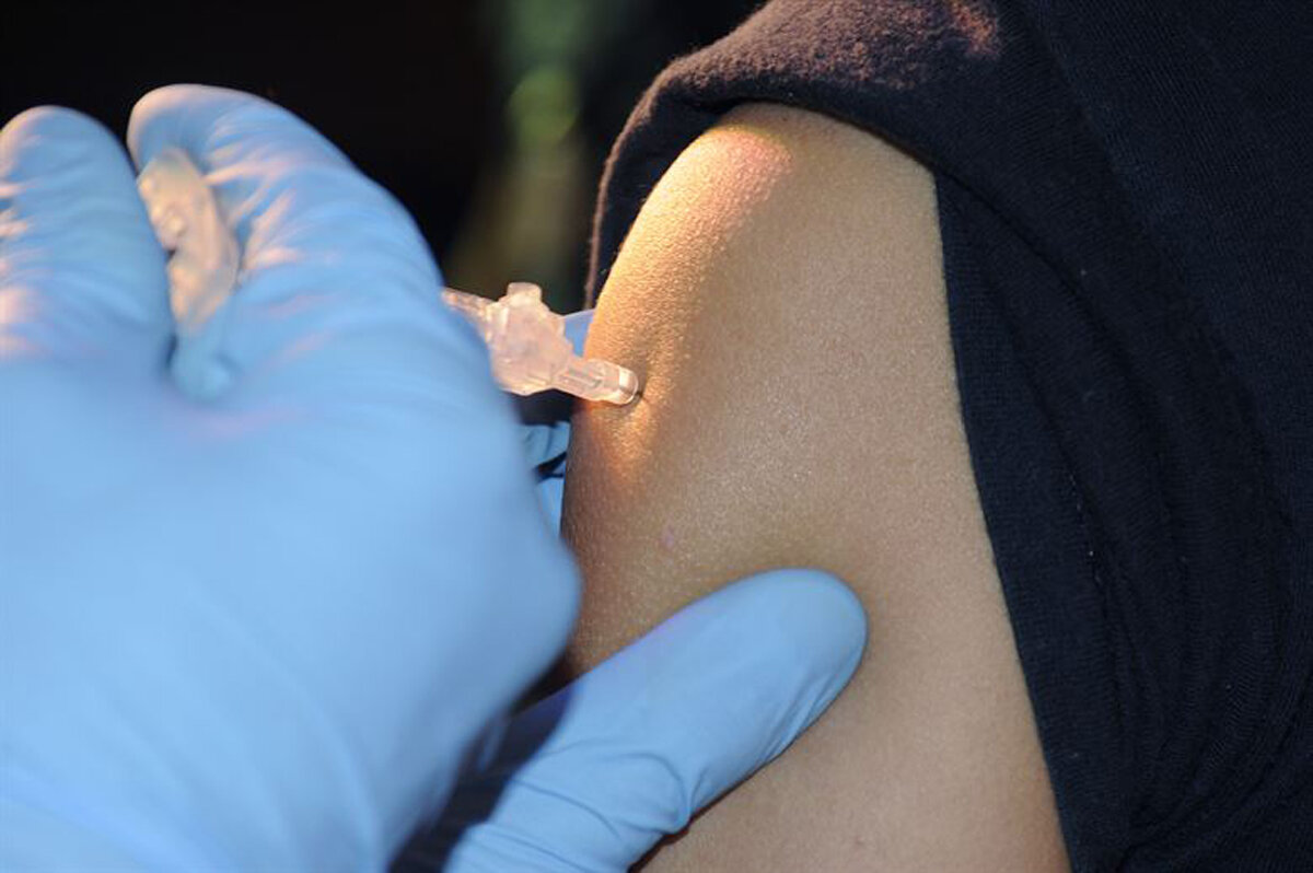 Healthcare worker administering an injection to a patient's upper arm.